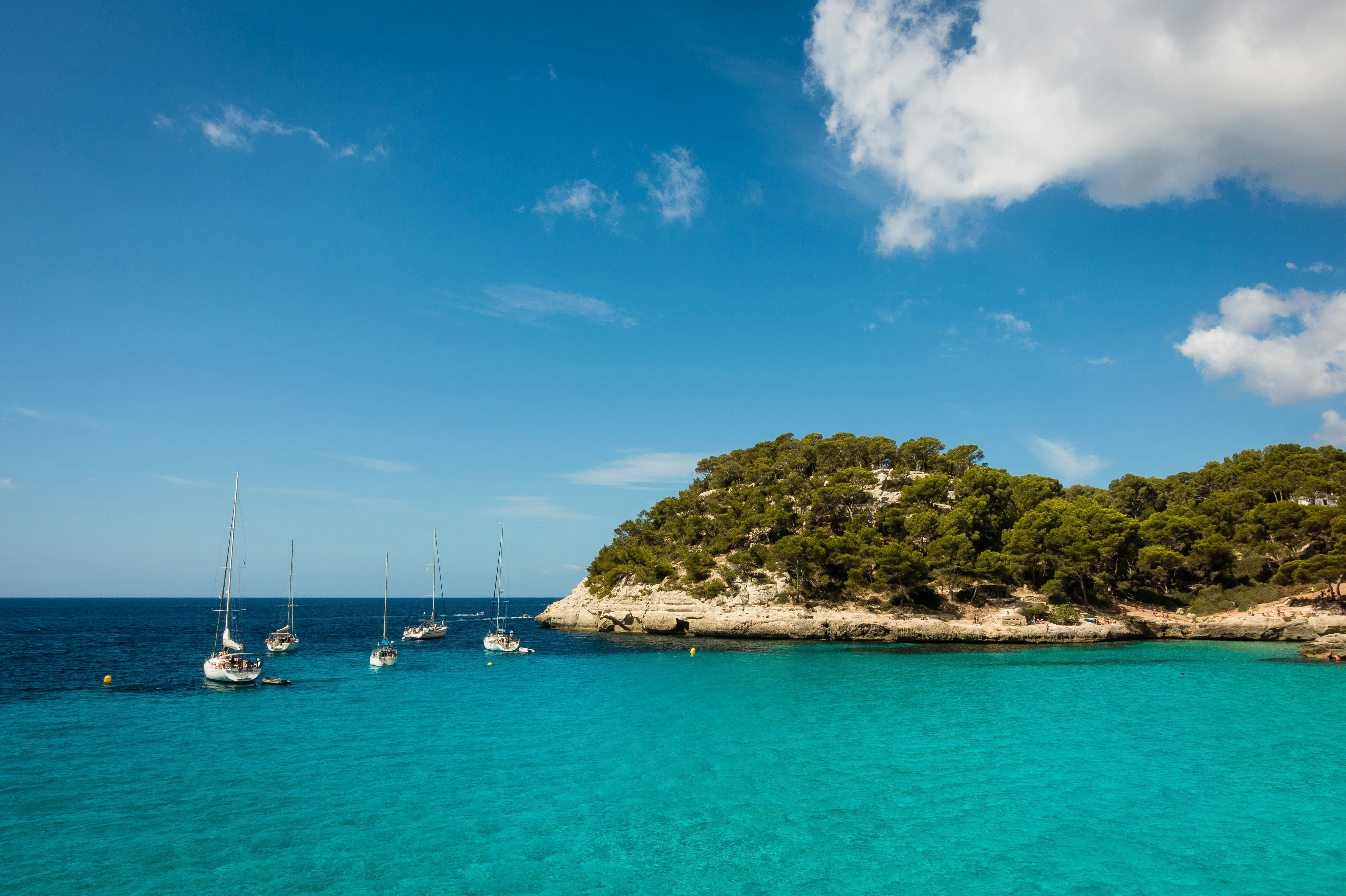 Crystal-clear cove in the Balearics with sailboats at anchor